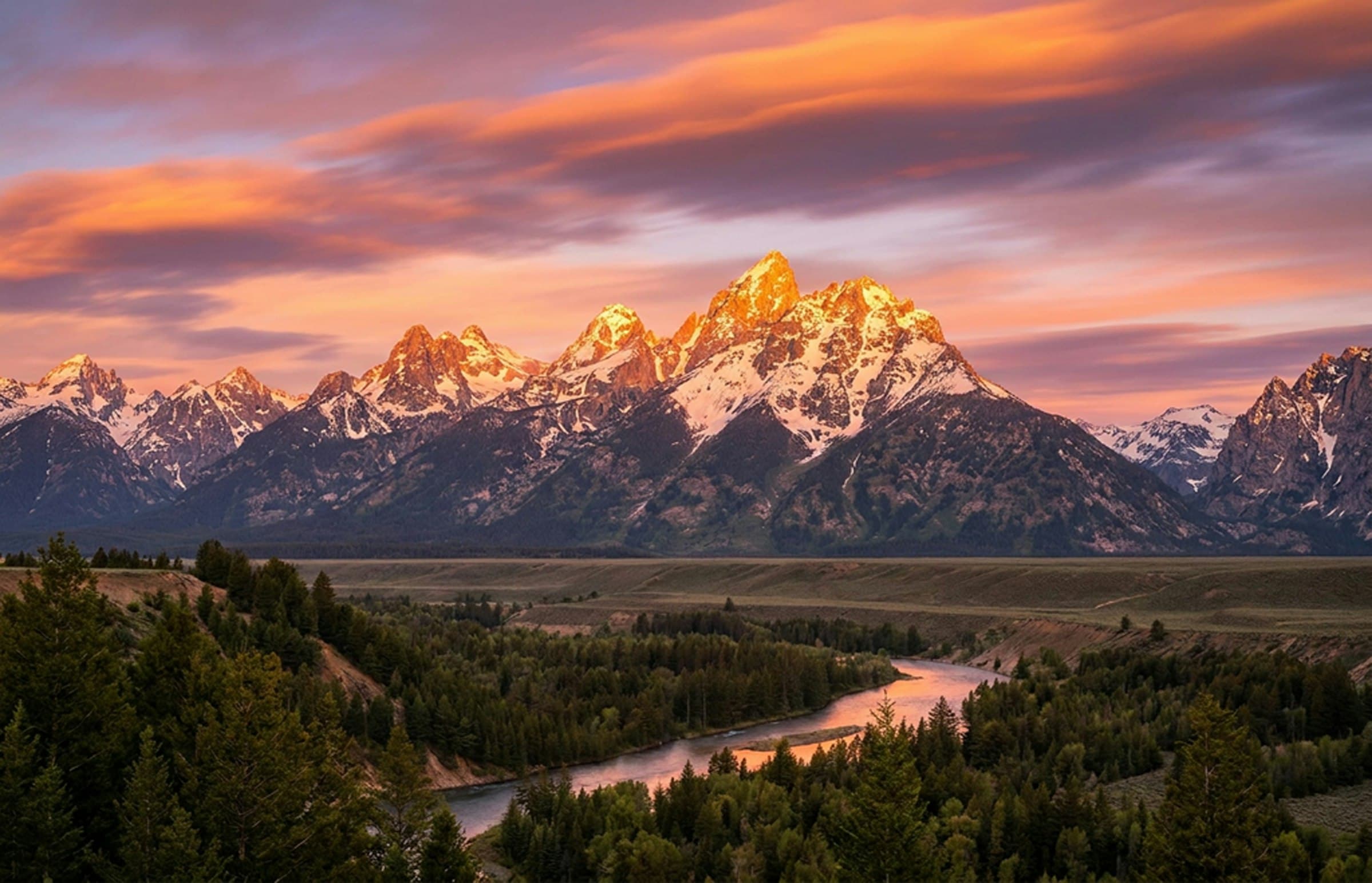 Alpenglow on a snow-capped mountain range above a winding river valley
